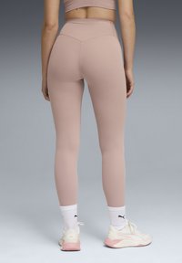 Leggings taille haute en tissu rose clair, avec un design sans coutures et une texture lisse, associés à des baskets blanches et des chaussettes de sport.