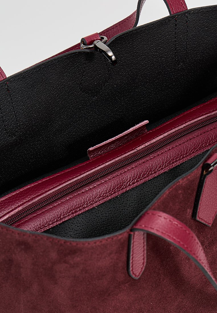 Burgunderfarbene Handtasche mit glattem Lederaußenmaterial und weichem Wildleder-Textur, ausgestattet mit einem schwarzen Innenfutter aus Stoff und einem Reißverschlussfach für Ordnung.