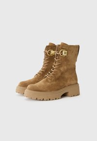 Bruine suède veterschoenen met een stevige zool, voorzien van accenten in goudkleurig beslag en een gestructureerde afwerking. Stevig ontwerp met enkelhoogte.