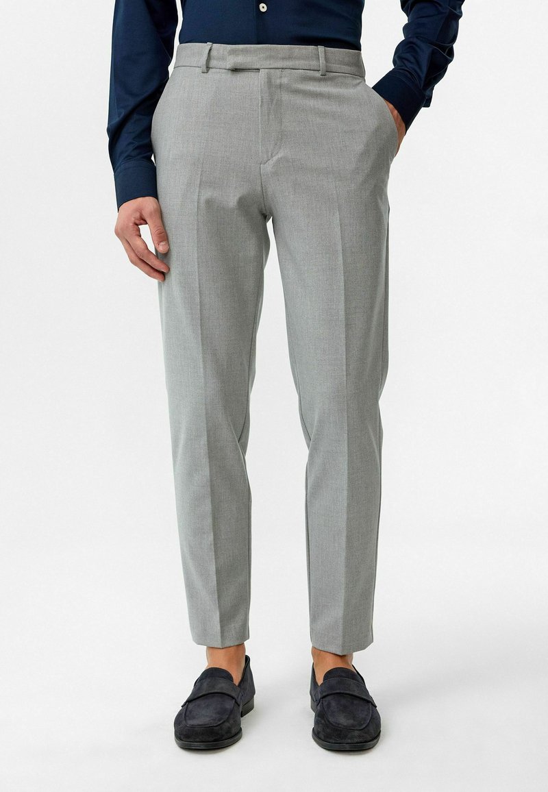 Lichtgrijze, op maat gemaakte broek met een vlakke voorkant, slim fit en subtiele textuur. Gecombineerd met donkere loafers. Geen zichtbare patronen of accenten.