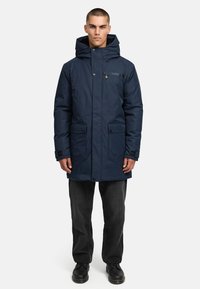 Jūras spēku garais parka jaka ar plašu kapuci, priekšējo rāvējslēdzēju, sānu kabatām un regulējamām piedurknēm. Izgatavota no gludas, teksturētas auduma.