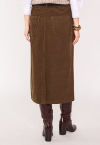 Gonna midi in velluto a coste marrone con taglio dritto, dotata di tasche posteriori e una texture liscia. Abbinata a stivali bordeaux al ginocchio.