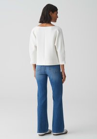 Pull blanc texturé avec un col bateau, associé à un jean bleu évasé. Le jean a un design classique à cinq poches et est légèrement décoloré.