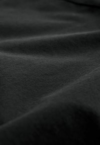 Schwarzer Stoff mit einer glatten, matten Textur, die sanfte Falten und subtile Lichtvariationen über die Oberfläche zeigt.