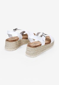 Sandales plateformes blanches avec des lanières croisées et une boucle en métal. Talon compensé enveloppé de jute et semelle intérieure en cuir marron doux. Semelle texturée pour une meilleure adhérence.