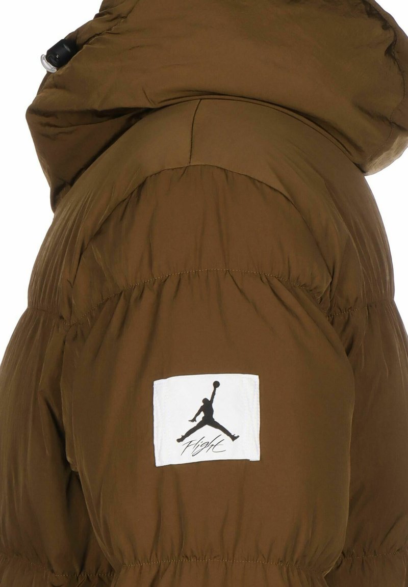 Braune Daunenjacke mit Kapuze. Mit einem auffälligen weißen Patch mit dem Jumpman-Logo und dem Text "Flight". Glatte, matte Textur.