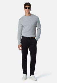 Grau strukturierter Pullover, schwarze Hose und weiße Sneaker; Model trägt Sonnenbrille. Einfaches Design mit Rundhalsausschnitt und taillierter Form.