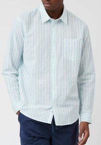 Camisa de rayas azul claro y blanca hecha de un tejido ligero. Presenta un cuello con botones y un bolsillo en el pecho. Manga larga con puños.