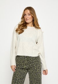 Béžový pletený sveter s okrúhlym v�ýstrihom a dlhými rukávmi, v kombinácii s olivovo zelenými nohavicami s leopardím vzorom. Jemná textúra, voľný strih.