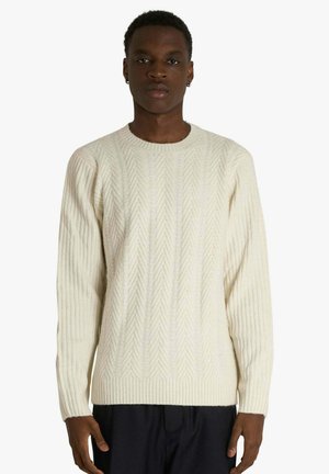 Maglione lavorato a maglia color crema con motivo a spina di pesce testurizzato, polsini a coste e scollo tondo. Vestibilità aderente con maniche lunghe.
