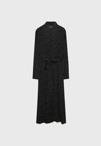 Robe midi noire à manches longues avec pois blancs, boutonnée devant, col et ceinture à nouer à la taille sur fond neutre.