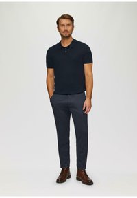Polo-shirt �à manches courtes marine, associé à un pantalon foncé à motifs et des bottes marron. Design simple, texture lisse et apparence ajustée générale.