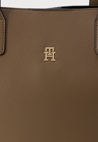 Geantă de umăr din piele maro cu o suprafață texturată. Dispune de un detaliu cu logo auriu la centru, mânere rezistente și un design elegant.