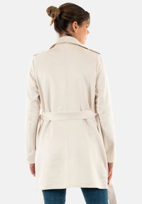 Trench coat color beige chiaro con vita sbloccata, maniche lunghe e colletto a punta. Texture liscia con dettagli di cucitura sul retro.