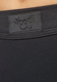 Svart bomullsresår med en sydd logolapp. Slät textur med fin ribb längs den övre kanten.