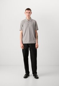 Lysegrå polo-skjorte med korte ermer og tre-knapps knappelukking, kombinert med svarte denim-bukser og svarte loafers, på en nøytral bakgrunn.