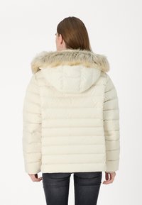 Doudoune en blanc cassé avec une capuche doublée en fausse fourrure. Design matelassé horizontal, manches longues et coupe décontractée.