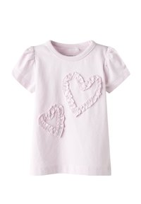 Camiseta de algodón rosa claro con mangas cortas abullonadas y dos aplicaciones en forma de corazón con volantes en un rosa ligeramente más oscuro. Textura suave.