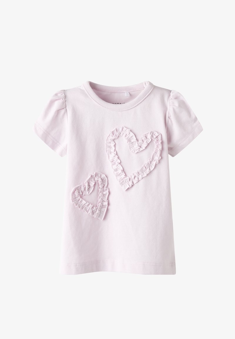 Camiseta de algodón rosa claro con mangas cortas abullonadas y dos aplicaciones en forma de corazón con volantes en un rosa ligeramente más oscuro. Textura suave.