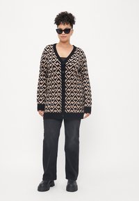 Brown and black patterned cardigan with a V-neck, button closure, and long sleeves, paired with black pants and chunky black boots.