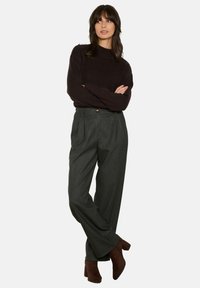 Tmavě hnědý pletený svetr s vysokým límcem, doplněný šedými kostičkovanými kalhotami s vysokým pasem. Celý outfit doplňují hnědé kožené kotníkové boty na podpatku.