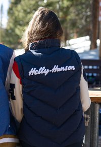 Granatowa kamizelka puchowa z przeszyciami w kształcie zygzaka i textured powierzchnią, z logo "Helly Hansen" w białym haftem na plecach.