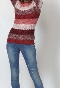 Sweter dzianinowy w czerwone, różowe i białe poziome paski, połączony z wysłużonymi niebieskimi dżinsami z haftem kwiatowym i postrzępionymi krawędziami.