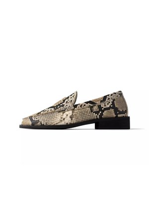 Loafer met lage hak met beige en zwart slangenhuidpatroon en een platte zwarte zool, gezien vanaf de buitenkant tegen een witte achtergrond.