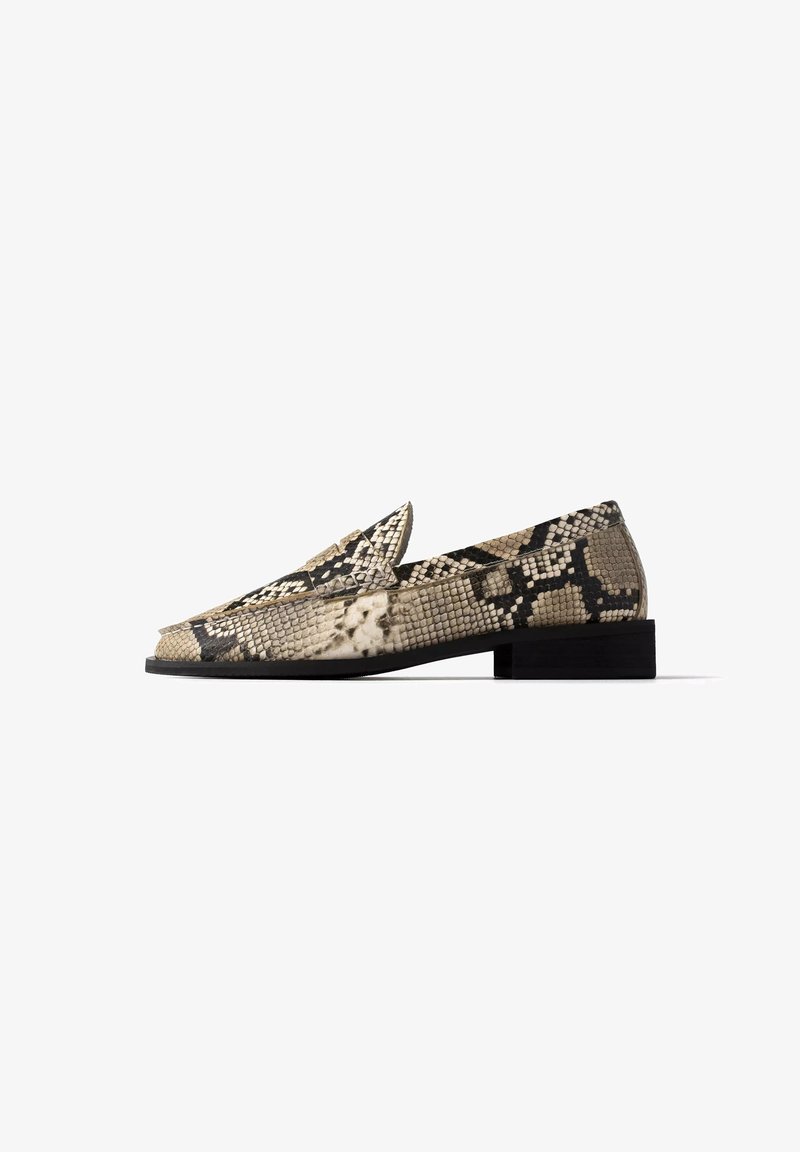Mocassin à talon bas avec un motif peau de serpent beige et noir et une semelle plate noire, vu de l'extérieur sur fond blanc.