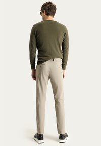 Suéter verde oliva y pantalones beige claros. Los pantalones tienen bolsillos traseros con costuras claras. Usados con zapatillas negras.