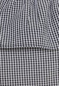 Tissu vichy noir et blanc avec un petit motif à carreaux, présentant une texture froncée en haut et une texture plate en bas.