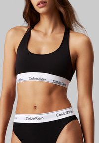 Fekete sportmelltartó és hozzá illő alsó, fehér elasztikus szalagokkal, melyeken a "Calvin Klein" logó található. Az anyag lágy és sima tapintású.