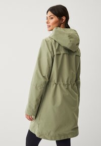 Olijfgroene waterdichte parka met capuchon, aantrekbare taille en een detail op de rug. Glad textuur en knielange snit.