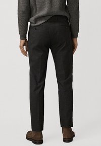 Donkergrijze op maat gemaakte broek met een gladde textuur, slim fit ontwerp en subtiele achterzakken, gecombineerd met bruine enkellaarzen.