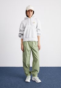 Gray hoodie with kangaroo pocket, green cargo pants, and light sneakers; model wearing a beige cap, set against a plain background.
