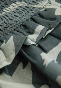 Tissu vert et beige à motifs avec texture plissée, doté de smocks élastiques et d'une drape douce et fluide. La vue en gros plan met en avant les détails.