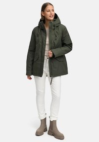 Green hooded jacket with pockets, cinched waist, and zipper closure. Paired with white jeans and taupe ankle boots, set against a neutral background.