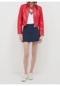 Rode cropped jas van nep leer met drukknopen, gecombineerd met een wit topje met een zwarte streep en een marineblauwe skort; witte sneakers.