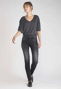 Blouse grise à col en V associée à un jean skinny gris foncé. Tissu lisse, coupe ajustée, et léger délavage sur le jean. Mocassins noirs complètent le look.
