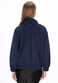 Marineblauw windjack met elastische manchetten en zoom. Voorzien van een hoge kraag en een zachte, gladde textuur. Minimalistisch ontwerp, geen zichtbare hardware.