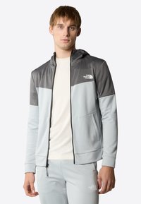 Giacca con cappuccio in tessuto a maglia grigio e azzurro chiaro con un motivo testurizzato. Presenta una chiusura frontale con zip e tasche doppie. Logo visibile sul petto.