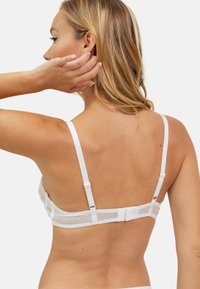 Soutien-gorge en dentelle blanche et en mesh avec un dos transparent, des bretelles ajustables et une fermeture à crochets. Texture lisse et détails de motif délicats.