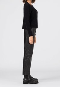 Svart fluffig tröja med V-hals, i kombination med högmidjade svarta läderbyxor och ankelstövlar. Sidan visar avslappnad passform och texturer.