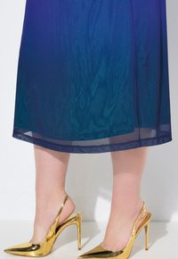 Scarpe gold con tacco alto, slingback, a punta, con superficie riflettente e tacco sottile, abbinate a una gonna trasparente di un blu profondo.