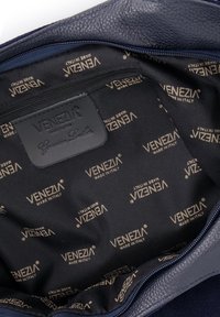Navy leren tas interieur met een zwarte stofvoering, voorzien van een herhaald "VENEZIA MADE IN ITALY" logo patroon en ritssluiting.