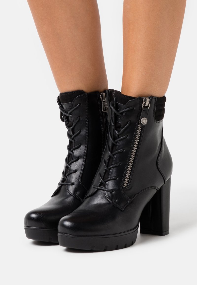 Bottines en cuir noir avec un laçage à l'avant, détail de fermeture éclair sur le côté, talons blocs hauts et accent en texture au niveau de la cheville.