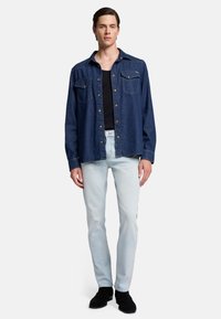 Dunkelblaue Jeanshemd mit zwei Brusttaschen, kombiniert mit hellblauen Jeans und schwarzen Schuhen. Schlichtes Design, lässiger Schnitt und Knopfverschluss.