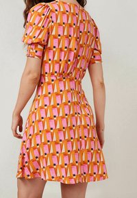 Robe à manches courtes présentant un motif géométrique coloré en rose, orange et noir. Confectionnée en tissu lisse avec une taille cintrée et une jupe évasée.