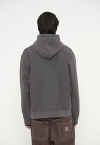 Hallide halliga hall sweatshirt mugava lõikega, siledast kangast ja ribaga mansettidega, koos pruunide pükstega, millel on tagakotid.