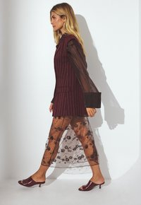 Blazer a righe bordeaux abbinato a una gonna in pizzo trasparente con motivi floreali e mule bordeaux con tacco basso.